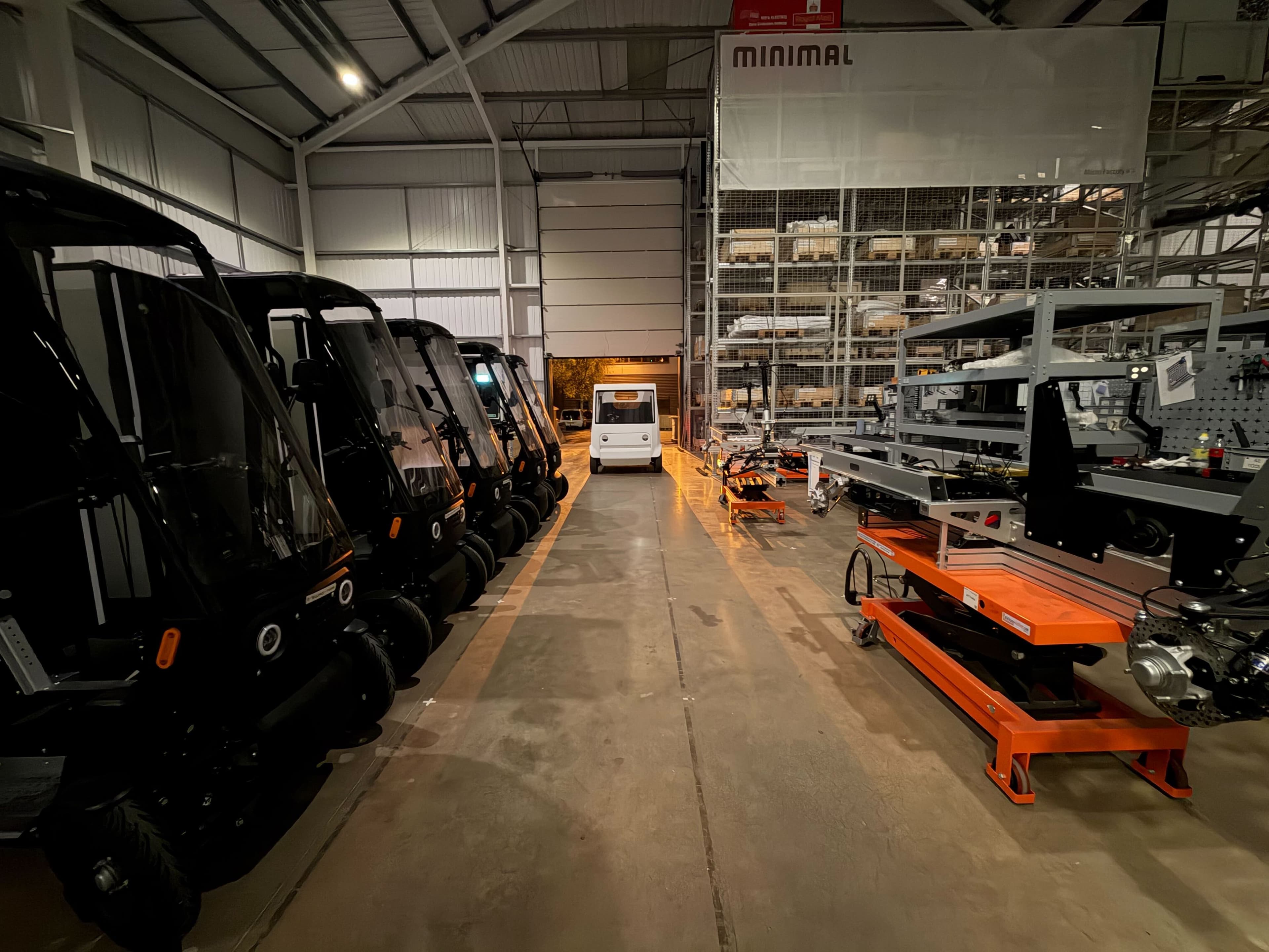 Inside the Minimal factory at night, a row of vehicles beside assembly equipment with one driving down the central aisle